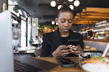 Geschäftsfrau benutzt Smartphone am Tisch in einem Cafe - PNAF05944