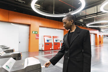 Junge Frau nimmt eine Fahrkarte aus einem Automaten in einer U-Bahn-Station - PNAF05968