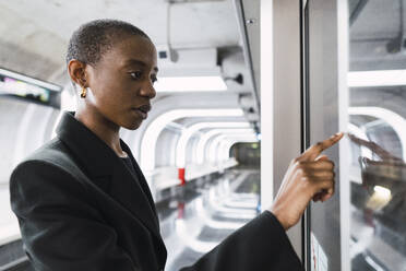 Junge Frau berührt digitale Anzeige in einer U-Bahn-Station - PNAF05974