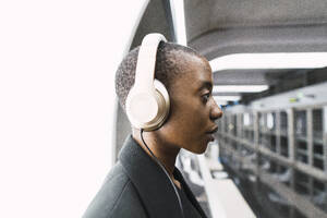Thoughtful woman wearing headphones at metro station - PNAF05984