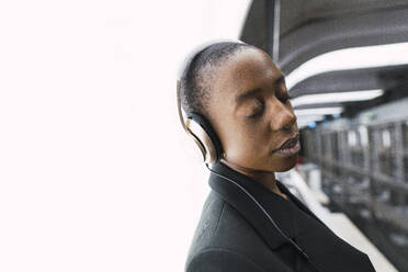 Junge Frau, die Kopfhörer trägt und sich mit geschlossenen Augen an eine U-Bahn-Station lehnt - PNAF05986