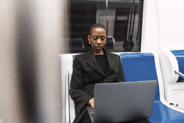 Junge Geschäftsfrau arbeitet an einem Laptop in der U-Bahn - PNAF05999