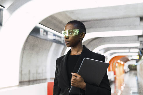 Nachdenkliche junge Frau mit einer intelligenten Brille und einem Laptop in einer U-Bahn-Station - PNAF06006