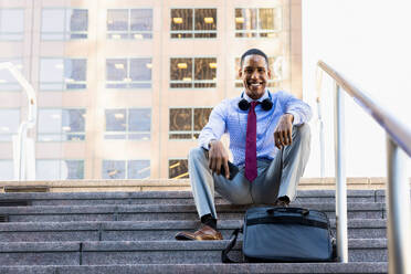 Gutaussehender afrikanischer Geschäftsmann, CEO, in einem eleganten Anzug in einem Geschäftszentrum im Freien - Schwarzer männlicher Pendler auf dem Weg zur Arbeit, Stadt und Finanzviertel im Hintergrund - DMDF01561