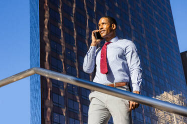 Gutaussehender afrikanischer Geschäftsmann, CEO, in einem eleganten Anzug in einem Geschäftszentrum im Freien - Schwarzer männlicher Pendler auf dem Weg zur Arbeit, Stadt und Finanzviertel im Hintergrund - DMDF01572