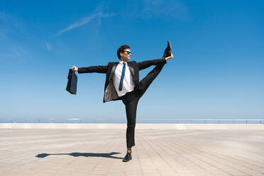 Happy and handsome adult businessman wearing elegant suit doing acrobatic trick moves in the city, alternative concept for business advertisement with energetic and creative people - DMDF01586