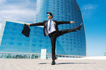 Happy and handsome adult businessman wearing elegant suit doing acrobatic trick moves in the city, alternative concept for business advertisement with energetic and creative people - DMDF01589