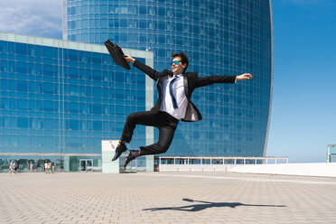 Happy and handsome adult businessman wearing elegant suit doing acrobatic trick moves in the city, alternative concept for business advertisement with energetic and creative people - DMDF01590