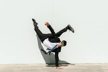 Happy and handsome adult businessman wearing elegant suit doing acrobatic trick moves in the city, alternative concept for business advertisement with energetic and creative people - DMDF01593