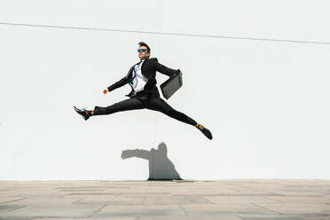 Happy and handsome adult businessman wearing elegant suit doing acrobatic trick moves in the city, alternative concept for business advertisement with energetic and creative people - DMDF01595