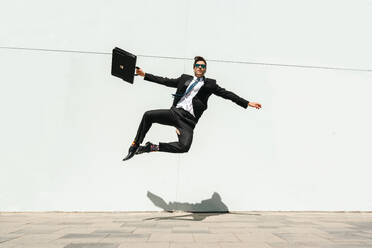 Happy and handsome adult businessman wearing elegant suit doing acrobatic trick moves in the city, alternative concept for business advertisement with energetic and creative people - DMDF01596
