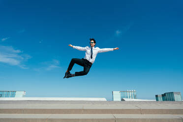 Happy and handsome adult businessman wearing elegant suit doing acrobatic trick moves in the city, alternative concept for business advertisement with energetic and creative people - DMDF01598