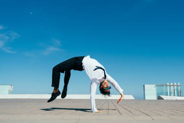 Happy and handsome adult businessman wearing elegant suit doing acrobatic trick moves in the city, alternative concept for business advertisement with energetic and creative people - DMDF01599