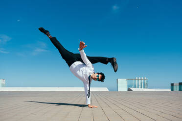 Happy and handsome adult businessman wearing elegant suit doing acrobatic trick moves in the city, alternative concept for business advertisement with energetic and creative people - DMDF01600