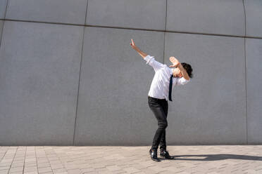 Happy and handsome adult businessman wearing elegant suit doing acrobatic trick moves in the city, alternative concept for business advertisement with energetic and creative people - DMDF01602