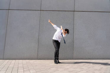 Happy and handsome adult businessman wearing elegant suit doing acrobatic trick moves in the city, alternative concept for business advertisement with energetic and creative people - DMDF01604