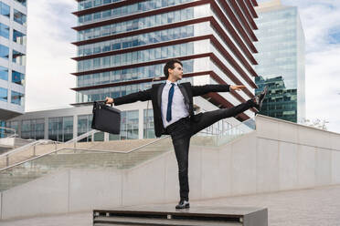Happy and handsome adult businessman wearing elegant suit doing acrobatic trick moves in the city, alternative concept for business advertisement with energetic and creative people - DMDF01606