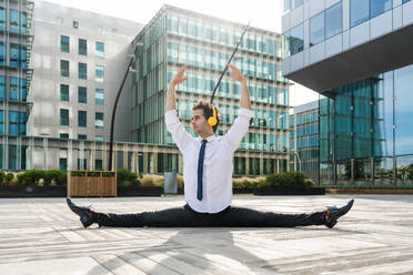 Happy and handsome adult businessman wearing elegant suit doing acrobatic trick moves in the city, alternative concept for business advertisement with energetic and creative people - DMDF01612