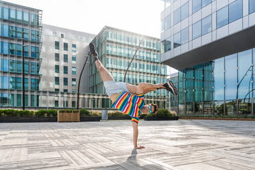 Happy and handsome adult man wearing colorful t-shirt doing acrobatic trick moves in the city, alternative concept for advertisement with energetic, playful and creative people - DMDF01618