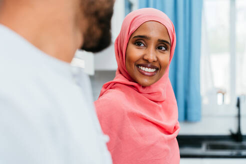 Happy middle-eastern couple wearing traditional arab clothing at home - Married arabian husband and wife bonding together in the apartment, concepts about relationship, domestic life and emirati lifestyle - DMDF01630