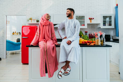 Happy middle-eastern couple wearing traditional arab clothing at home - Married arabian husband and wife bonding together in the apartment, concepts about relationship, domestic life and emirati lifestyle - DMDF01640