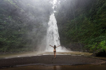 Beautiful young woman posing at the great Sekumpul waterfall in the deep rainforest of Bali island, Indonesia. - DMDF01680