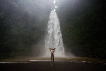 Beautiful young woman posing at the great Sekumpul waterfall in the deep rainforest of Bali island, Indonesia. - DMDF01681