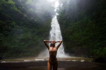 Beautiful young woman posing at the great Sekumpul waterfall in the deep rainforest of Bali island, Indonesia. - DMDF01682