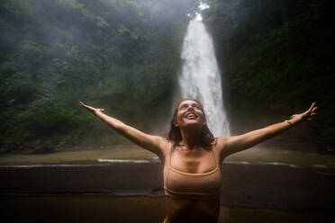 Beautiful young woman posing at the great Sekumpul waterfall in the deep rainforest of Bali island, Indonesia. - DMDF01683