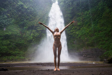 Beautiful young woman posing at the great Sekumpul waterfall in the deep rainforest of Bali island, Indonesia. - DMDF01686
