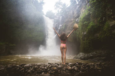 Schöne junge Frau posiert am großen Tegenungan-Wasserfall im tiefen Regenwald der Insel Bali, Indonesien. - DMDF01691