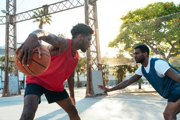 One vs one basketball game training at the court. Cinematic look image of friends practicing shots and slam dunks in an urban area - DMDF01790