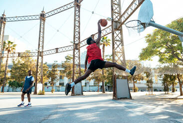 Junger Basketballspieler, der auf dem Platz trainiert. Filmische Darstellung eines Mannes, der in einem städtischen Gebiet Schüsse und Slam Dunks übt - DMDF01791