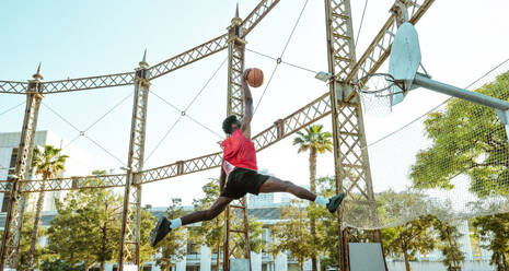 Junger Basketballspieler, der auf dem Platz trainiert. Filmische Darstellung eines Mannes, der in einem städtischen Gebiet Schüsse und Slam Dunks übt - DMDF01792