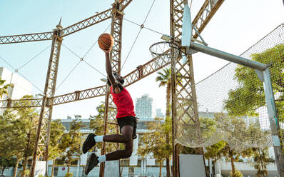 Junger Basketballspieler, der auf dem Platz trainiert. Filmische Darstellung eines Mannes, der in einem städtischen Gebiet Schüsse und Slam Dunks übt - DMDF01794
