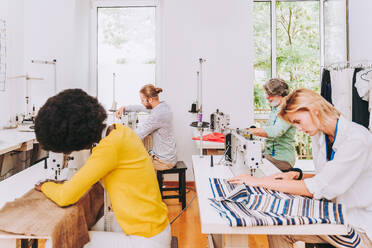 Multiethnisches Team von Modedesignern bei der Arbeit in einem Bekleidungs-Start-up-Workshop - Multirassische Gruppe von Stylisten, Schneidern und Schneiderinnen bei der Arbeit an einer neuen Kollektion - DMDF01825