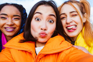 Multiracial group of young happy friends meeting outdoors in winter, wearing winter jackets and having fun - Multiethnic millennials bonding in a urban area, concepts about youth and social releationships - DMDF01930