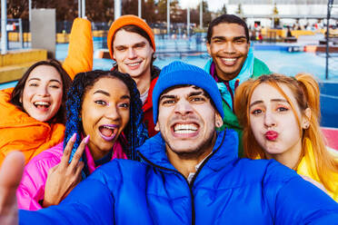 Multiracial group of young happy friends meeting outdoors in winter, wearing winter jackets and having fun - Multiethnic millennials bonding in a urban area, concepts about youth and social releationships - DMDF01937