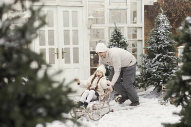 Vater fährt seine Tochter auf einem Schlitten vor dem Haus mit - ONAF00617