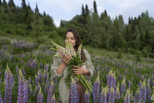 Serene woman smelling bunch of lupine flowers in field - VBUF00330