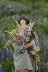 Serene women smelling bunch of lupine flowers in field - VBUF00331