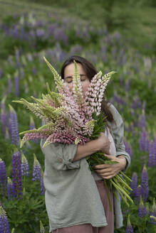 Gelassene Frauen riechen an einem Strauß Lupinenblüten auf einem Feld - VBUF00331