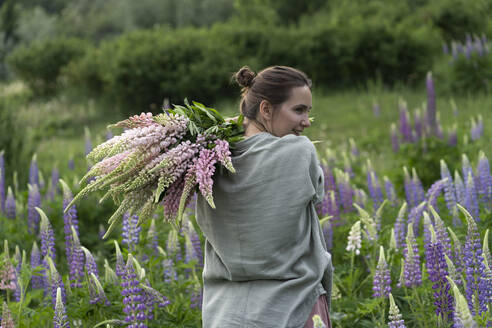 Glückliche Frau hält einen Strauß Lupinenblüten auf einem Feld - VBUF00332