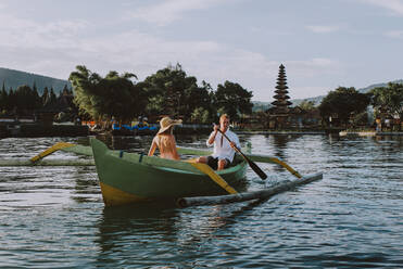 Junges hübsches Paar paddelt auf einem Holzboot bei Pura Ulun Danu Bratan, Bali - Touristen erkunden Bali - DMDF01970