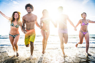 Multi-ethnic group of friends running on the beach - Young people having fun in the sea during summer holidays - DMDF02014