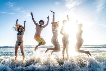 Multi-ethnic group of friends jumping on the beach - Young people having fun in the sea during summer holidays - DMDF02015