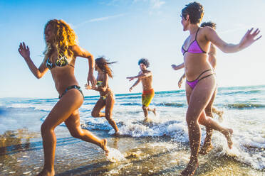 Multi-ethnic group of friends running on the beach - Young people having fun in the sea during summer holidays - DMDF02016