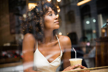 Beautiful afro woman sitting in a coffehouse - Pretty middle aged girl drinking coffee in a bar, reflection effect from window glass - DMDF02053