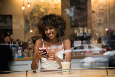 Beautiful afro woman sitting in a coffehouse - Pretty middle aged girl drinking coffee in a bar, reflection effect from window glass - DMDF02055