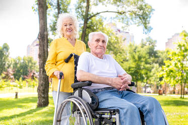 Beautiful senior couple with disability outdoors - Old people in the age of 60, 70, 80 having fun and spending time together, concepts about elderly, seniority, healthcare and wellness aging - DMDF02114